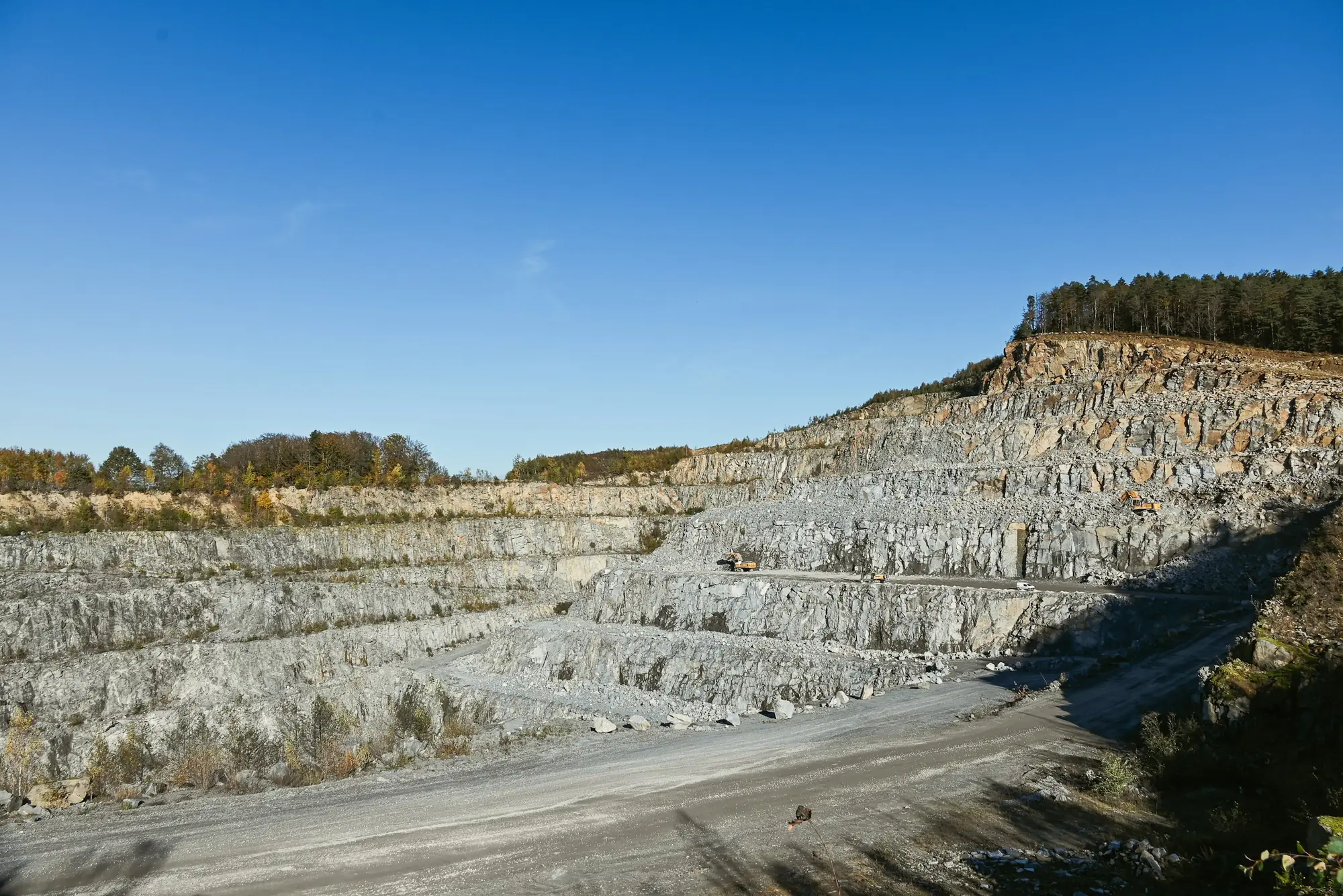 Terraced grey rock faces and a haul road in an open quarry under a clear blue sky